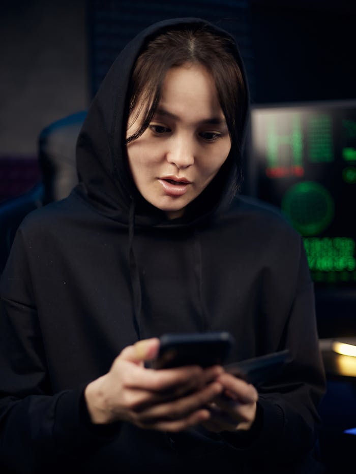 pexels-photo-7534098 A young woman in a black hoodie uses her smartphone indoors, surrounded by tech gear.
